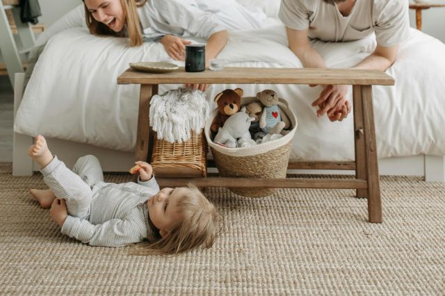 Family bonding time in a cozy bedroom with parents playing with child on the floor.
