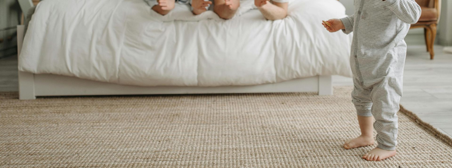 A joyful morning with parents encouraging their young child in a cozy bedroom setting.