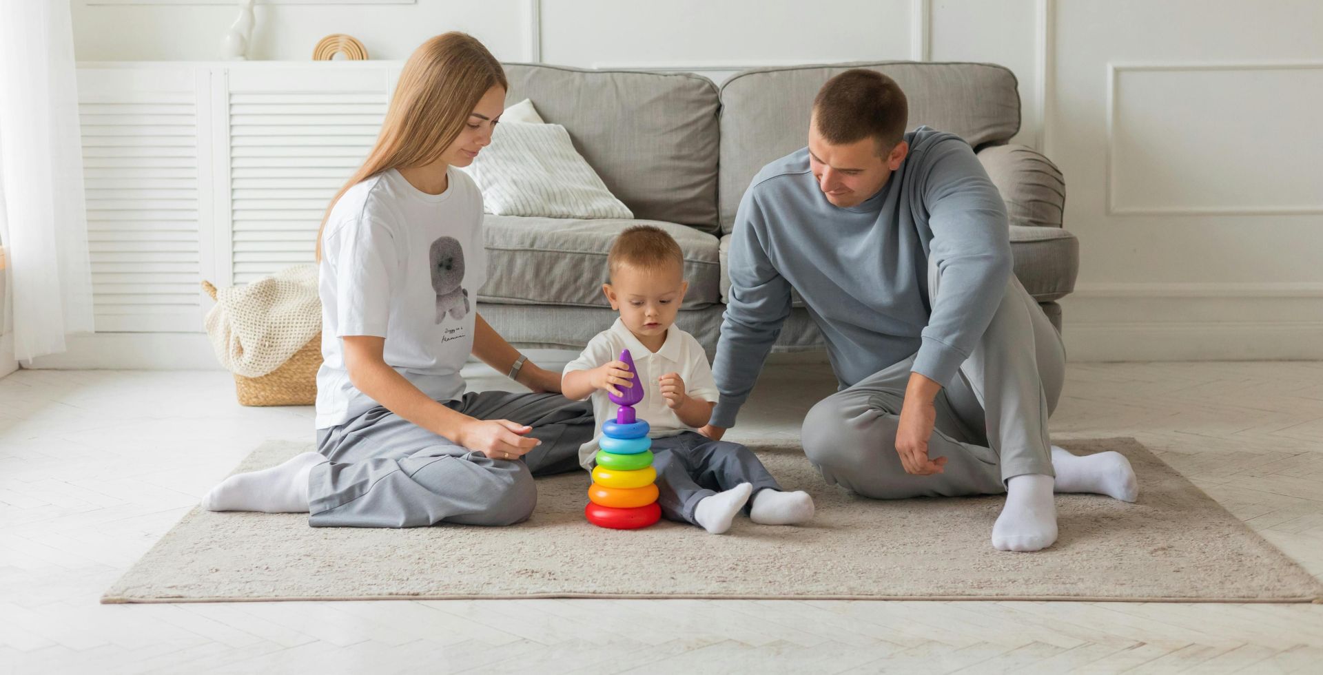 Mom, dad, and young child playing with colorful stacking toy in cozy living room setting.