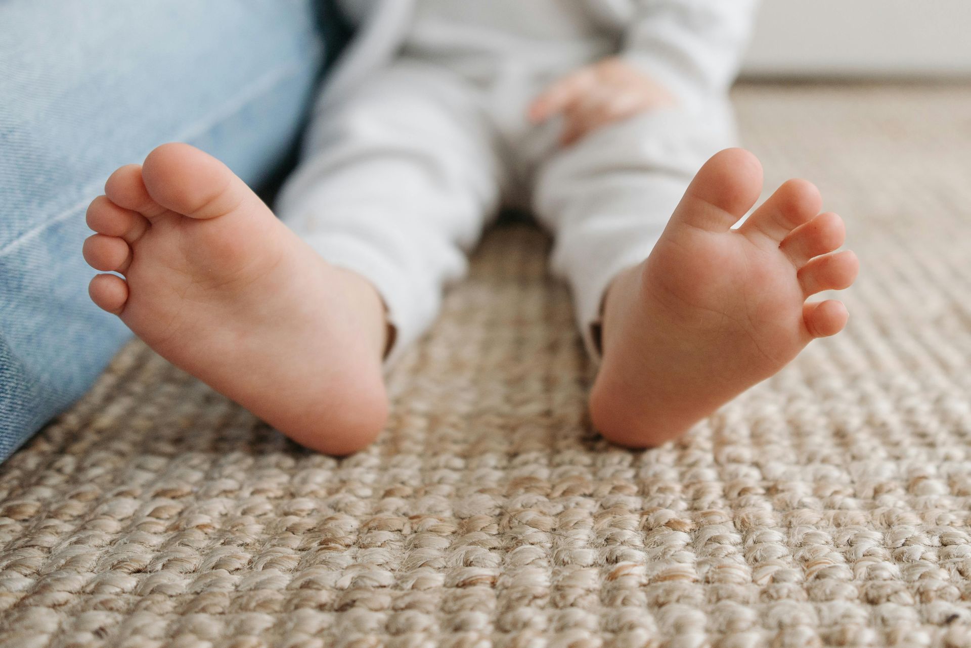 Adorable close-up of a child's bare feet resting on a textured carpet indoors.